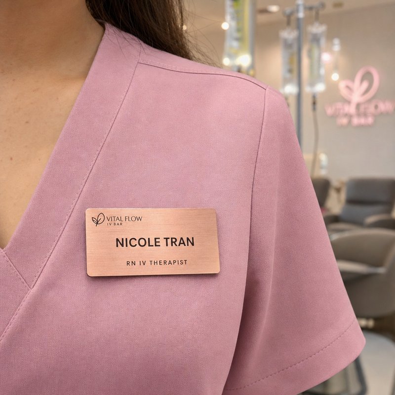 Brushed rose gold name badge worn on pink scrubs at an IV drip bar